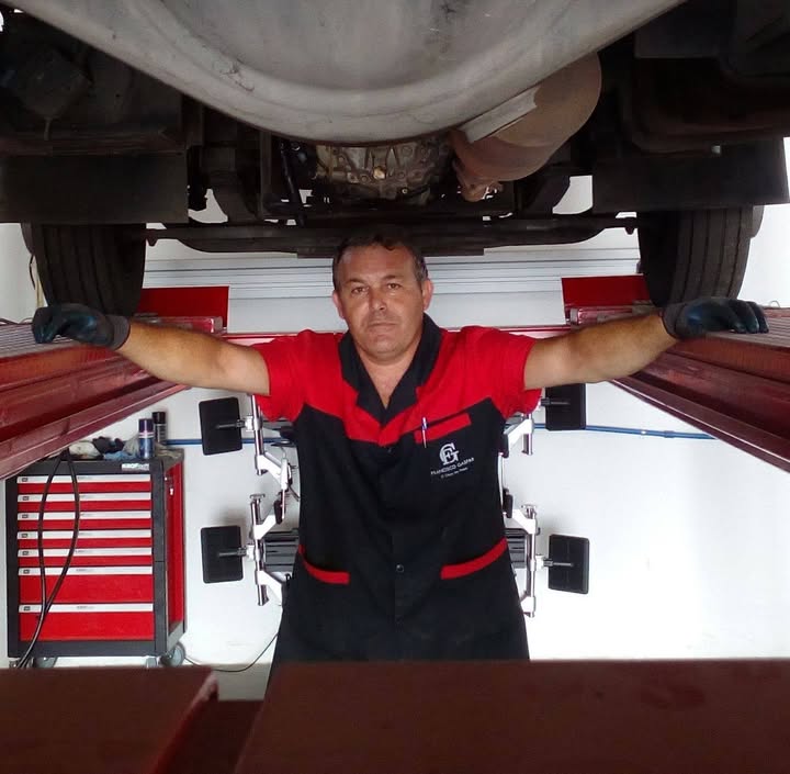 Profissional com uniforme Francisco Gaspar a trabalhar sob um automóvel elevado na oficina